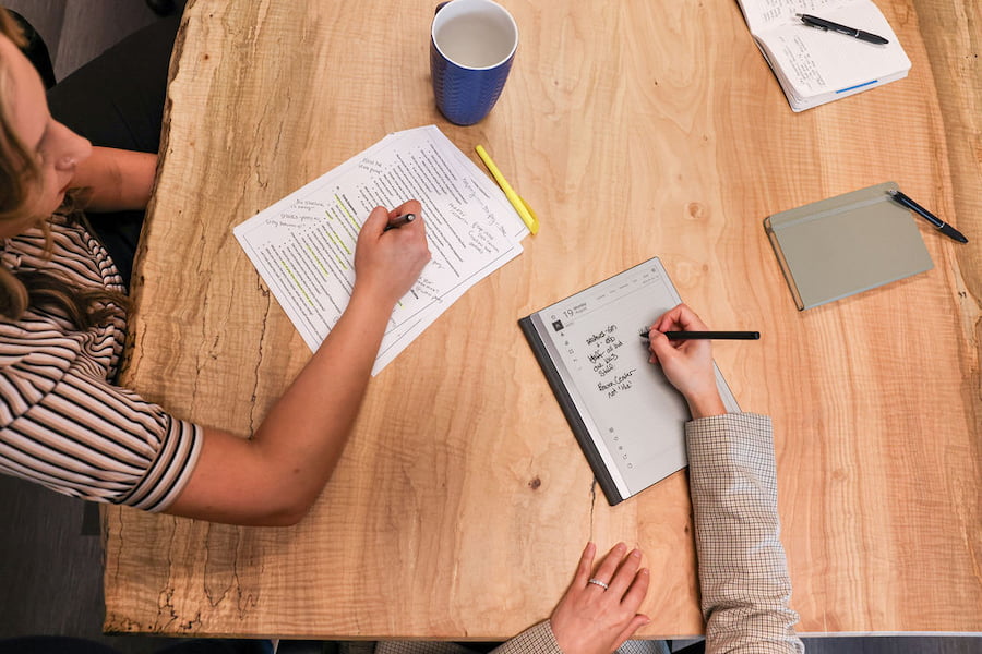 top-down view of employees making notes on their reports at a meeting