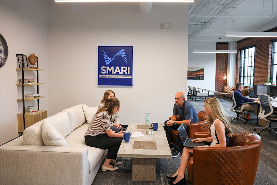 4 employees have a quick meeting at the SMARI lounge area in the office