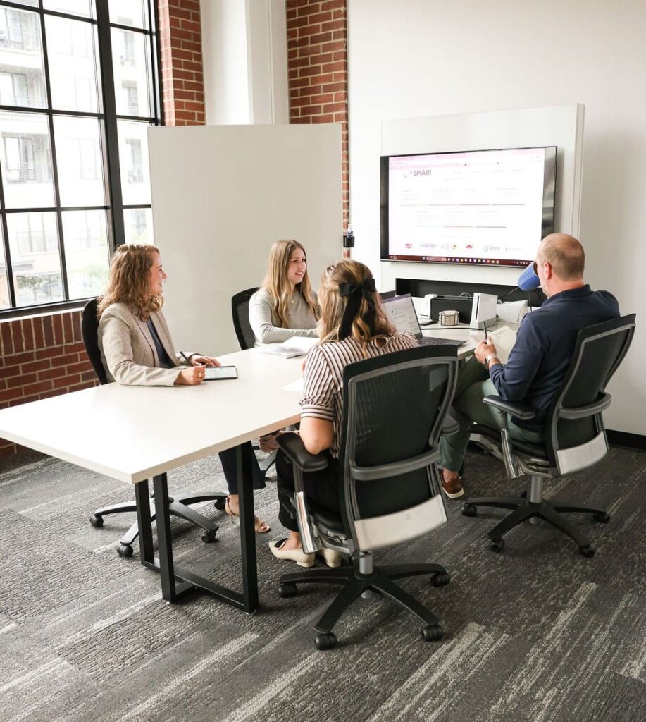 SMARI employees in their bright, open conference room looking at their work on a large monitor